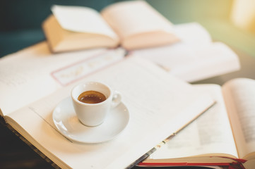 front view Cup of espresso among a lot of opened books sun light in background