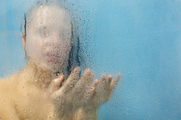 Naked female model takes bath in shower cabine, catches drops, relaxes under hot water, feels rest and relief, care of her skin, enjoys free time. Fresh young woman stands behind blurred glass