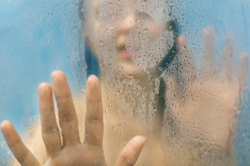 Woman`s silhouette touches glass with water drops, draws heart, stands in shower cabine alone, takes care of her beauty, has fun alone. People, freshness, hygiene, cleaning and bathing concept