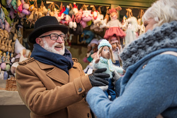 Fototapeta na wymiar This is for you. Excited old man is giving small cute toy to his wife. They are entertaining at fair outside