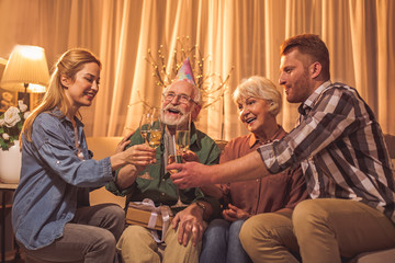 Glad relatives feasting in apartment. They tasting alcohol while sitting on sofa. Toast concept