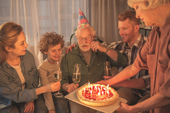 Cheerful grandfather celebrating birthday with beaming family . He looking at pie. Party concept