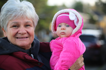 Happy family, generation and people concept - happy smiling young tree years old granddaughter with senior grandmother standing by House at Autumn Season, hugging in Oregon USA close-up portrait 