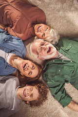 Top view portrait of laughing woman with son, smiling grandmother and granddad locating on carpet....