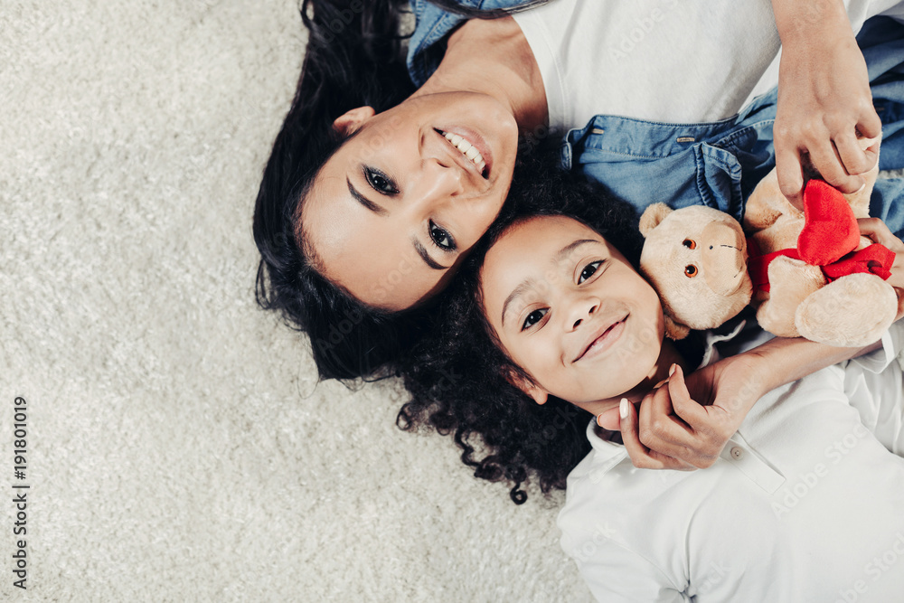 Poster top view portrait of content mother and child resting on rug with teddy bear. copy space in left sid