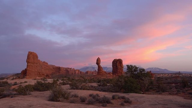 Wide panning view of Balanced Rock in Arches during colorful sunset in the Utah desert.