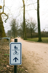 Sign indicating direction of bicycle and walking path in a park with blurred trees on the background