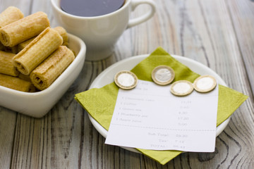 Pay restaurant bill. Bill, bank card, coins near cup of coffee on light wooden table top view