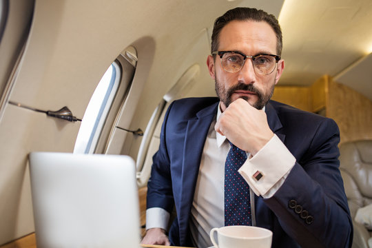 Portrait of serious handsome male in aircraft cabin sitting in his seat and looking at camera