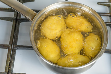 Untreated potatoes boil in a pot on a gas stove.