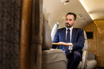 Naklejka na ściany i meble Waist up portrait of tranquil businessman sitting in comfortable seat of airplane at tray table. Copy space in left side