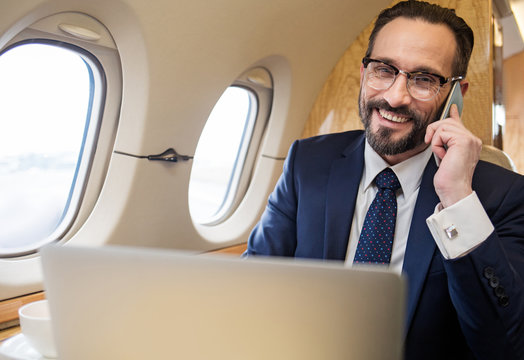 Portrait of contented gentleman in suit chatting by cellphone during his first class flight
