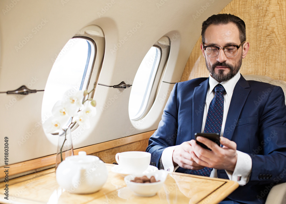 Poster waist up portrait of tranquil middle aged man travelling by plane. he is texting message on mobile p