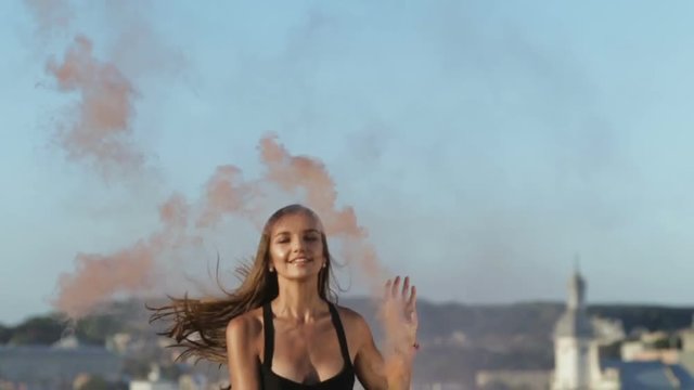 happy young woman having fun colorful powder cloud girl jumping orange color smoke bomb trampoline beauty fashionable bodysuit naked legs outside city horizon background smile free fresh modern art