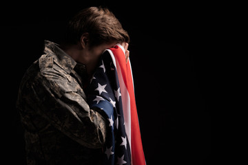 Despondent military man covering his face with hands and holding usa flag. Concept of despair....