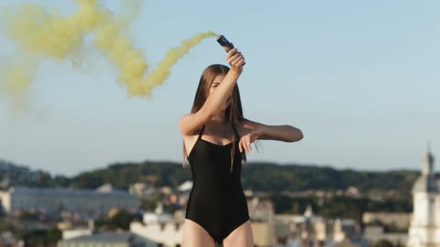 young brunette woman bicini swimsuit outside roof building lighting colored bomb yellow smoke throwing feather having fun jumping trampoline appy moment enjoyment active lifestyle great impression