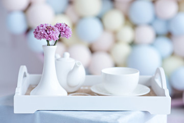 Breakfast in bed. White teapot with a cup of tea on a wooden tray with flowers.