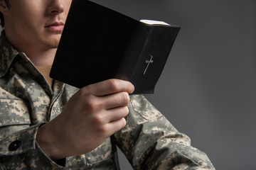 Male soldier holding the Bible in his hand and reading it. He is wearing military uniform. Isolated on grey background