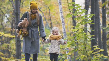 Little daughter with her mother and Teddy Bear walking in autumn park