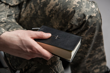 Close up of male hand holding the Bible. Disabled male veteran sitting and praying. He is wearing...