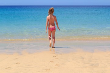 Fototapeta na wymiar Young girl on the beach are going to the sea, Fuerteventura- Canary Islands