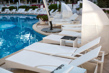 Interior of summer club with pool. Hotel pool. Resort Pool Club. Tourist resort. Pool with clean water, sun beds, folded tents, greens trees, flowers. Chaise lounges in swimming pool.