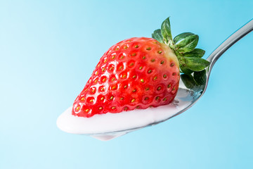 Strawberry on a spoon with strawberry pink yogurt cream close-up on blue background