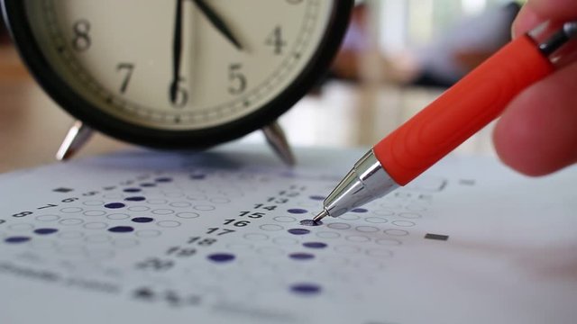Students taking exams writing on optical form of standardized exam near Alarm clock with  holding yellow pen for final examination in secondary school, college university classroom, Education concept