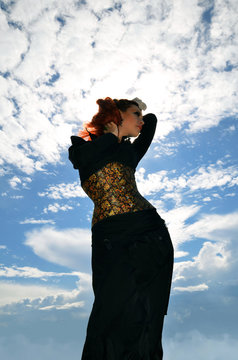 silhouette of a slender redheaded woman in a black dress and corset on a background cloudy sky