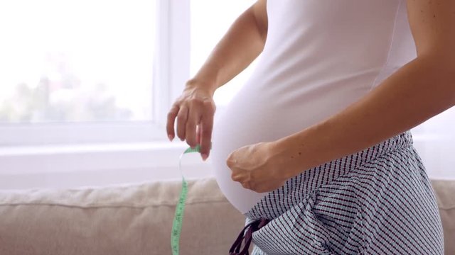 Pregnant woman measuring her belly with tape measure