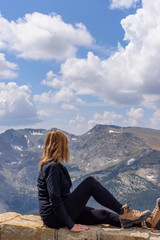 Fototapeta premium woman sitting on ledge looking out at rocky mountain range