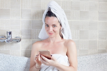 Mixed raced  young beautiful model with towel on her head sitting in bath tube and checking mail in...