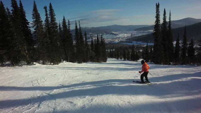 Woman in colorful orange sportswear is skiing on the slope of mountain at sunny winter day