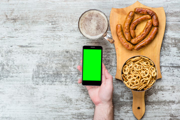 Male hand holding smartphone mobile cell phone near beer and snacks, food delivery order app application concept