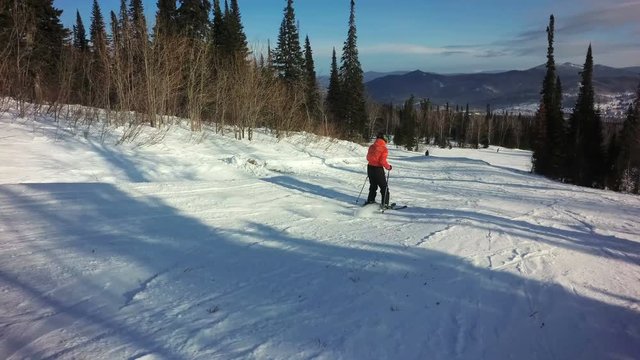 Woman in colorful orange sportswear is skiing on the slope of hill at sunny winter day