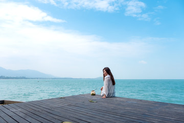 A beautiful asian woman on white dress sitting at the terrace with sea and blue sky background with feeling relaxed