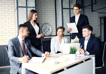 Brainstorm. Group of business people looking at the laptop together. One business woman looking at camera.