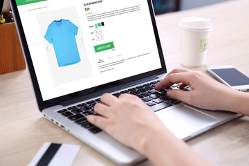 People buying running shirt on ecommerce website with smart phone, credit card and coffee on wooden...