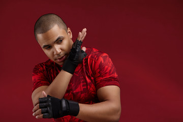 Sports and martial arts concept. Horizontal shot of strong young African boxer wearing red t-shirt and thai boxing training fingerless gloves mastering skills in gym, having focused facial expression