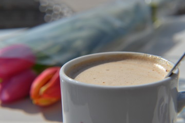 Warm cup of coffee and colorful tulips in background
