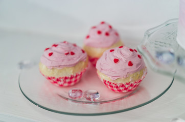 three pink muffins with red hearts on a transparent plate
