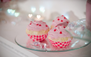 three pink cakes with red hearts on a transparent plate. Bokeh in the form of hearts