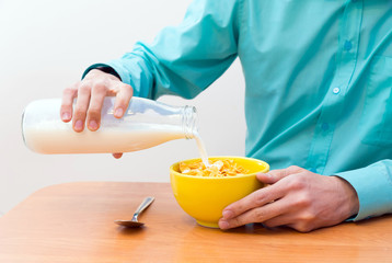 Obraz na płótnie Canvas Closeup of man's hands pouring milk into a yellow bowl of cornflakes