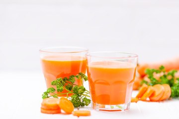 Carrot juice in beautiful glasses, cut orange vegetables and green parsley on white wooden background. Fresh orange drink. Close up photography. Selective focus. Horizontal banner