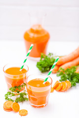 Carrot juice in beautiful glasses, cut orange vegetables and green parsley on white wooden background. Fresh orange drink. Close up photography. Selective focus. Vertical banner