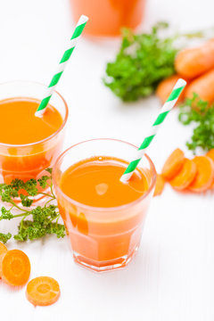 Carrot juice in beautiful glasses, cut orange vegetables and green parsley on white wooden background. Fresh orange drink. Close up photography. Selective focus. Vertical banner