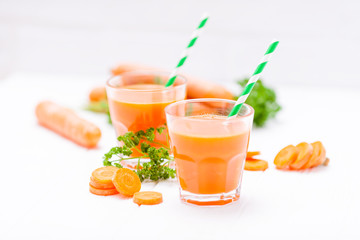 Carrot juice in beautiful glasses, cut orange vegetables and green parsley on white wooden background. Fresh orange drink. Close up photography. Selective focus. Horizontal banner