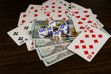 Playing cards, dice and one hundred dollar bills on a dark wooden table