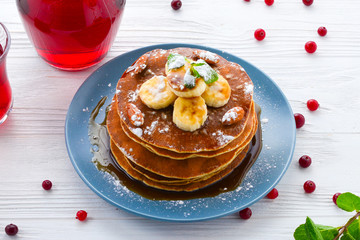 Pancakes with caramel, banana and nuts decorated with cranberries and mint with juice.