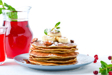 Pancakes with caramel, banana and nuts decorated with cranberries and mint with juice.